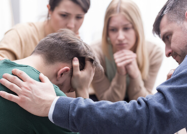 Erwachsene stehen einem verzweifelten jungen Mann zur Seite.